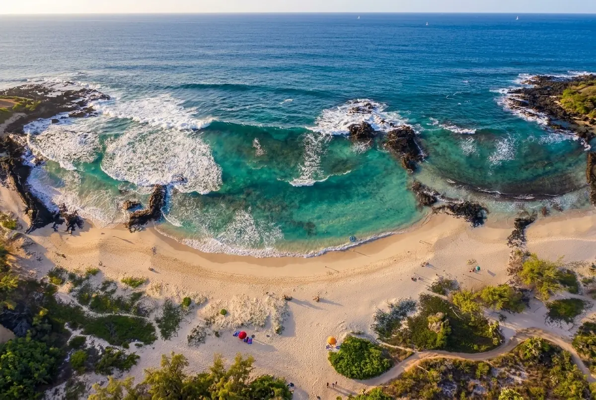Aerial view of a turquoise bay with white surf, black lava rock and a sandy beach on the Kona coast