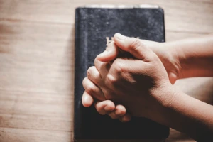 Hands folded in prayer on top of a Bible