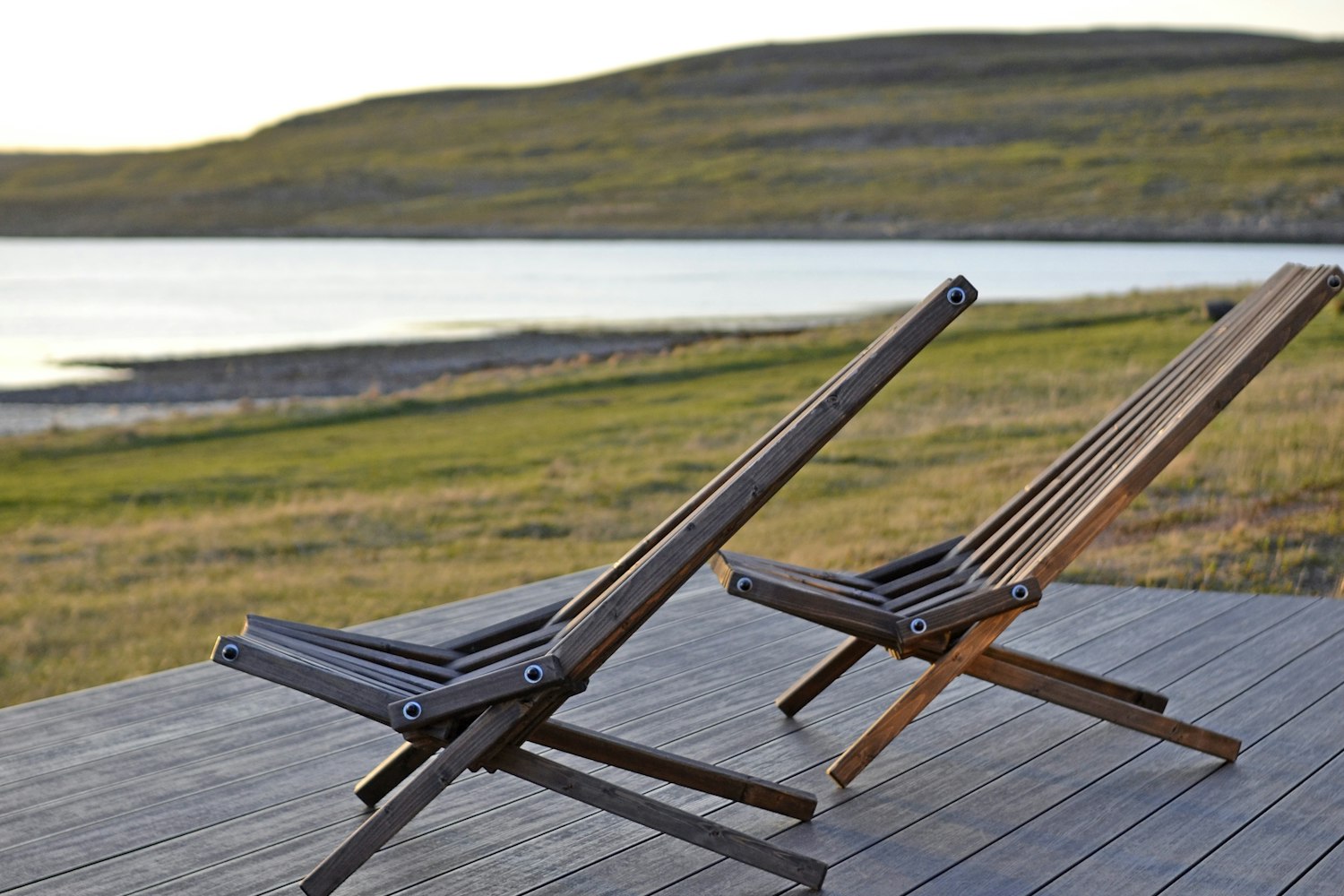 Two timber deck chairs on the weathered deck, turned to face open water across the headland.